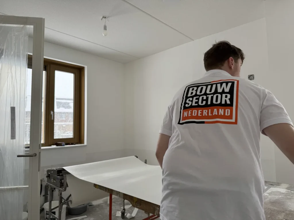 Behanger in wit shirt van Bouwsector Nederland rolt een baan vlies uit over de plaktafel