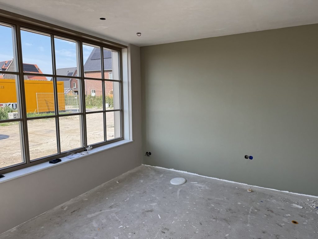 Kamer met een wand in een grijsgroene kleur naast een groot raam met roeden