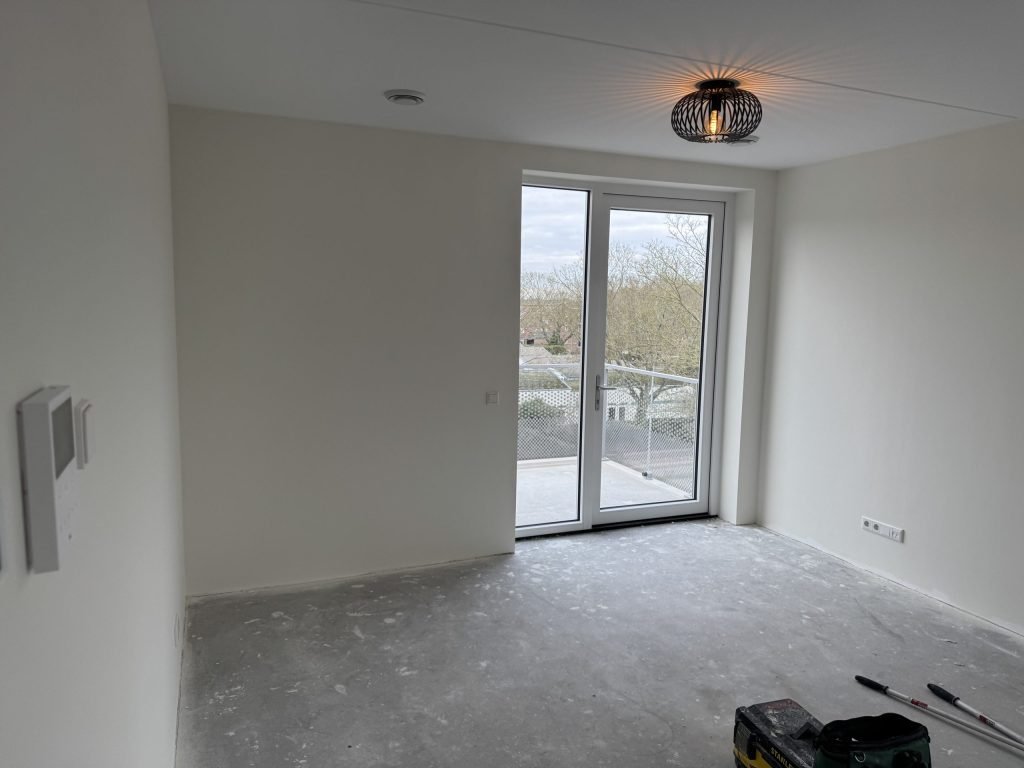 Lege kamer in een nieuw appartement met balkondeuren en lichte wanden, kort na de oplevering